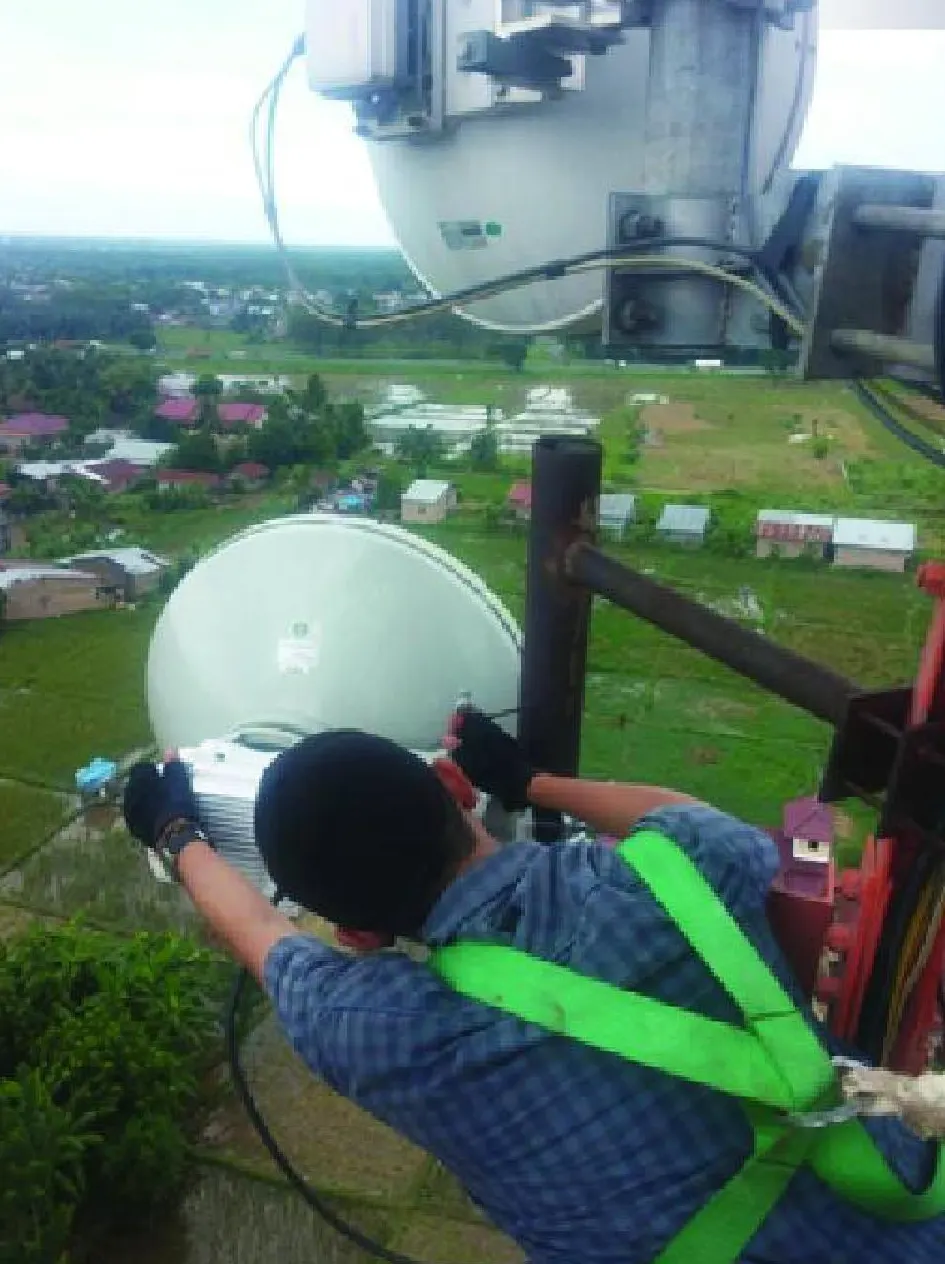 Teknisi dengan full body harness memasang radio wireless di ketinggian